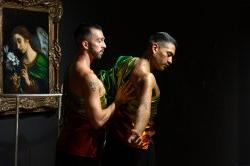 两个穿着闪亮绿色衣服的舞者, 黄金, 身穿红色服装，在卡洛·多尔奇的《天使加布里埃尔》和约瑟夫·利亚特拉以PULSE夜总会的栏杆为原型创作的作品前表演. 背景是暗哑光的黑色.