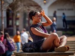 Photo of a female student sitting on a campus with her hand up shielding her eyes from the sun
