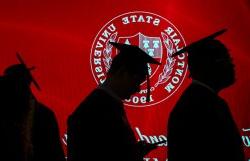 学生们戴着毕业帽，穿着毕业服，在带有十大博彩推荐排名州立大学印章的红色背景上勾勒出剪影.