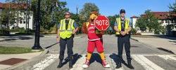 Picture of the Red the Red Hawk with two University Police Officers on a campus crosswalk.